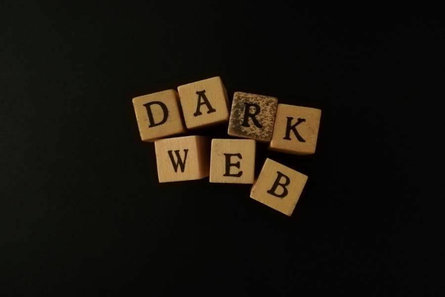 Des cubes en bois sombres avec des lettres noires forment les mots "DARK WEB" sur un fond noir uni pour illustrer ce concept mystérieux.