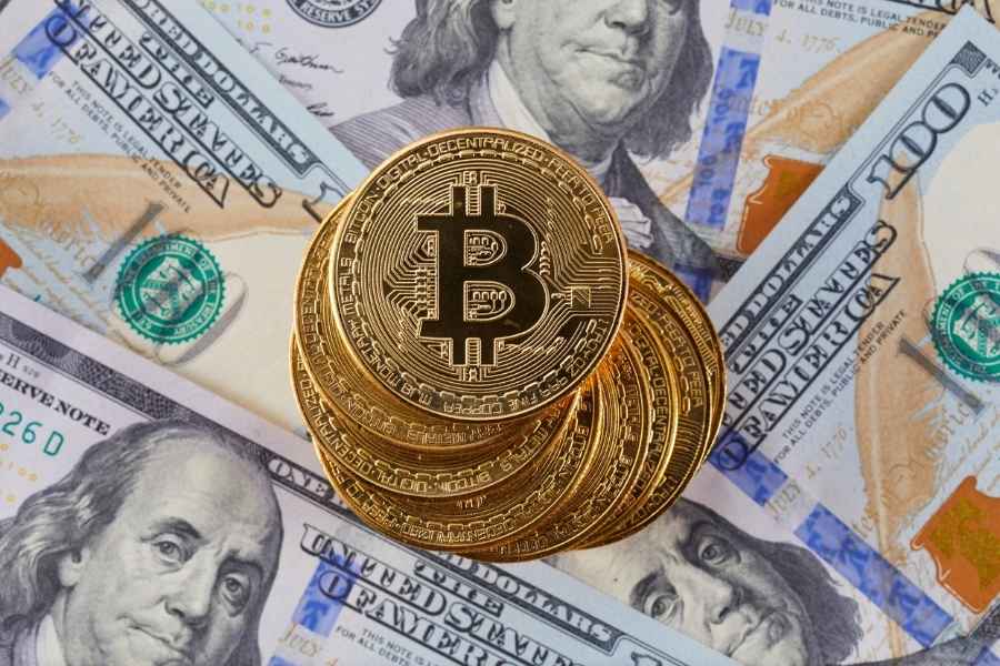 Un empilement de pièces de Bitcoin dorées posées sur des billets de banque américains pour illustrer l'univers de la blockchain.