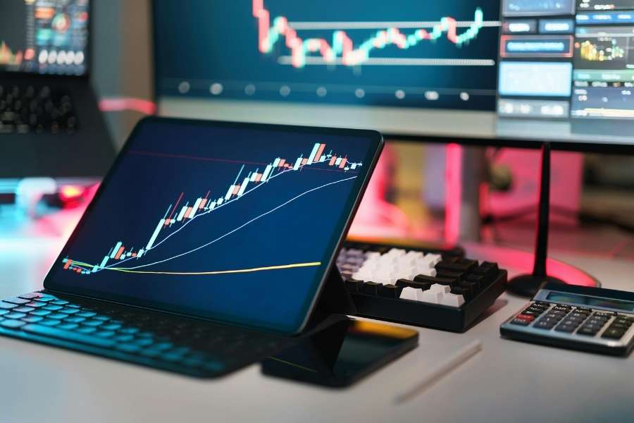 Une tablette et des écrans affichant des graphiques boursiers pour analyser le minage de Bitcoin.